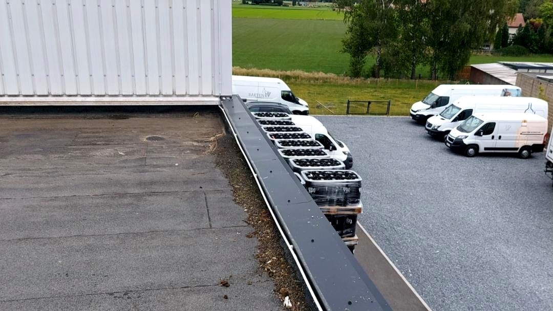 Grindparking met witte bestelwagens naast een magazijn, gezien vanaf het platte dak