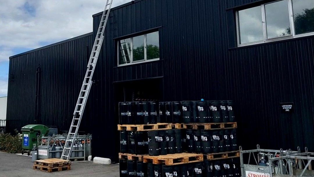 Ladder tegen de donkere metalen gevel van een magazijn, met paletten met vaten op de voorgrond