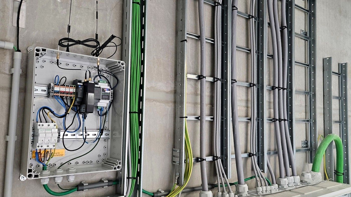 Geopende EMS-kast met gateway en RS485-omvormer aan de wand van een technische ruimte, naast kabelladders
