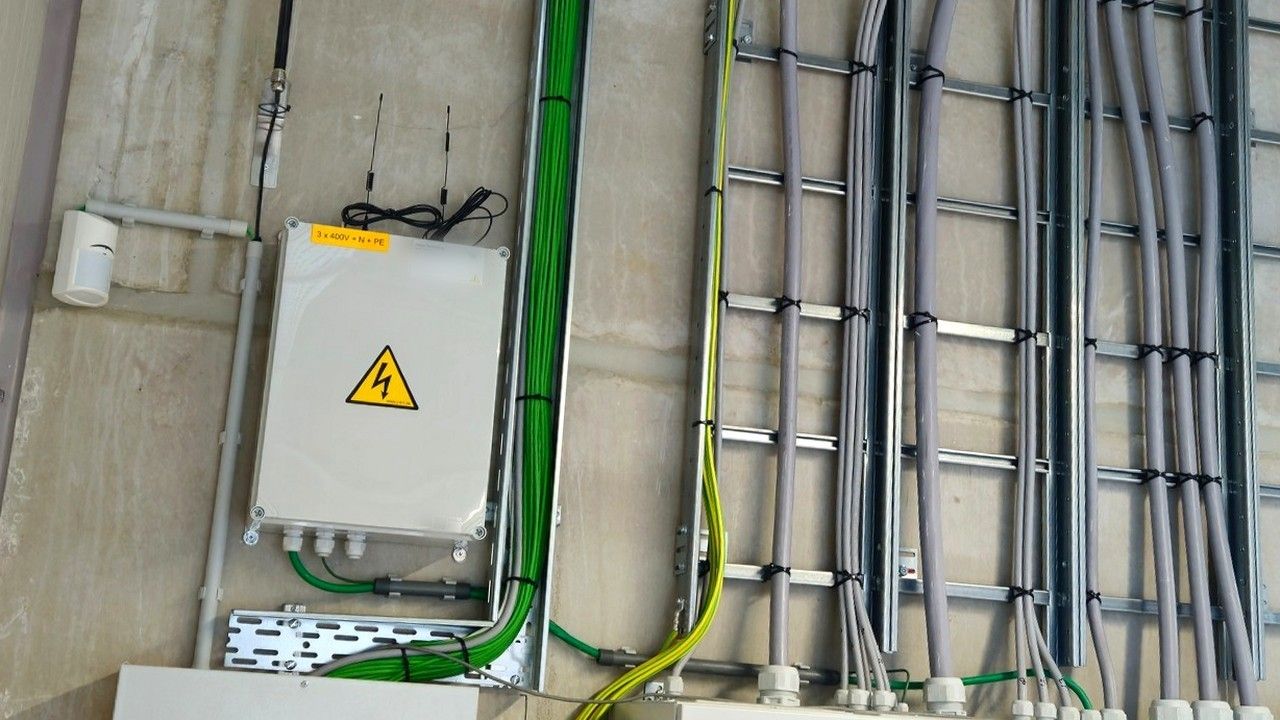 Gesloten grijze EMS-kast met antennes aan een betonwand naast kabelladders