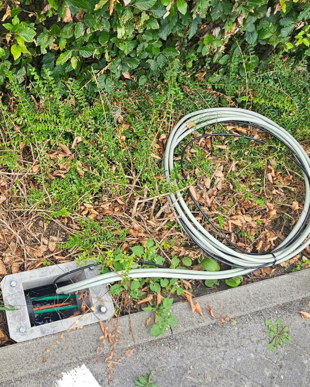 Metalen funderingskader in de grond met opgerolde voedingskabels naast een stoeprand