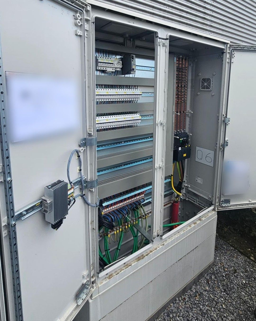 Geopende buitenverdeelkast met rijen automaten en binnengebrachte kabels onderaan