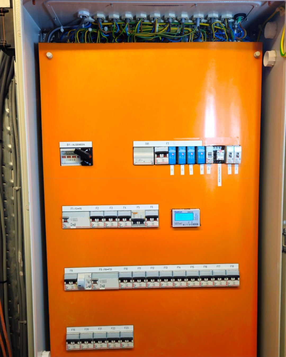 Verdeelbord met oranje afdekplaat, gelabelde automaten en een energiemeter