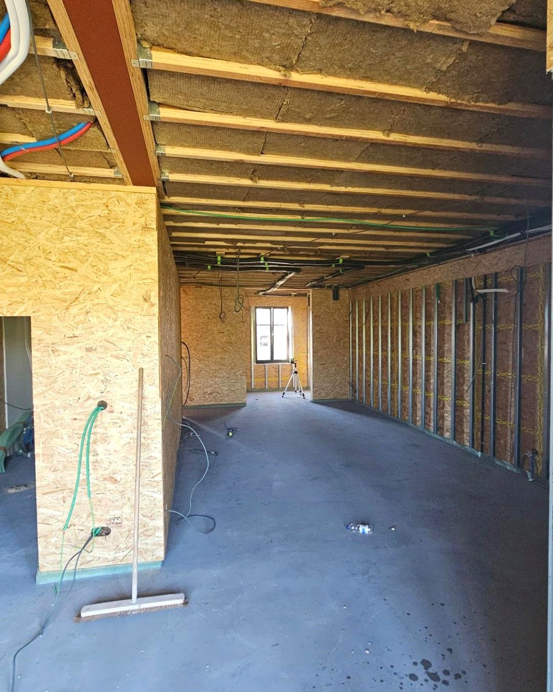 Lange open ruimte in houtskeletbouw met een nieuwe dekvloer, OSB-wanden en leidingen tegen het plafond