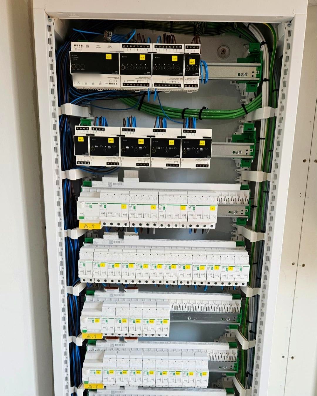 Geopend verdeelbord met gelabelde Niko Home Control-modules en rijen automaten, bekabeld met groene kabels